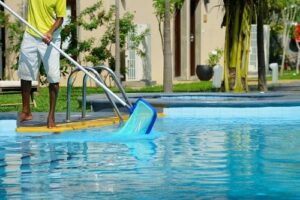 Pool technician is scooping leaves out of a swimming pool.